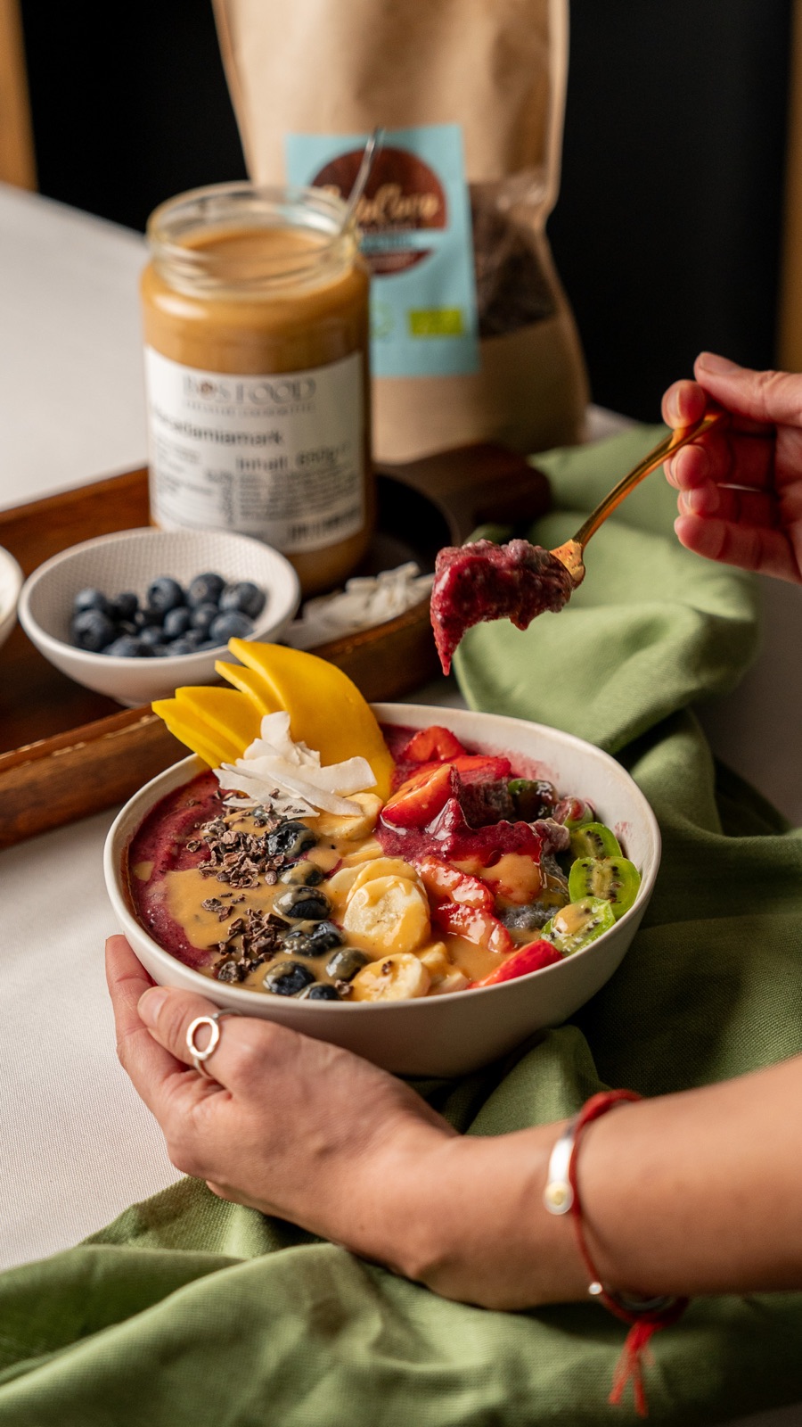 Löffel mit tiefvioletter Açaí-Masse über der Bowl, im Hintergrund BOS FOOD Macadamiamark